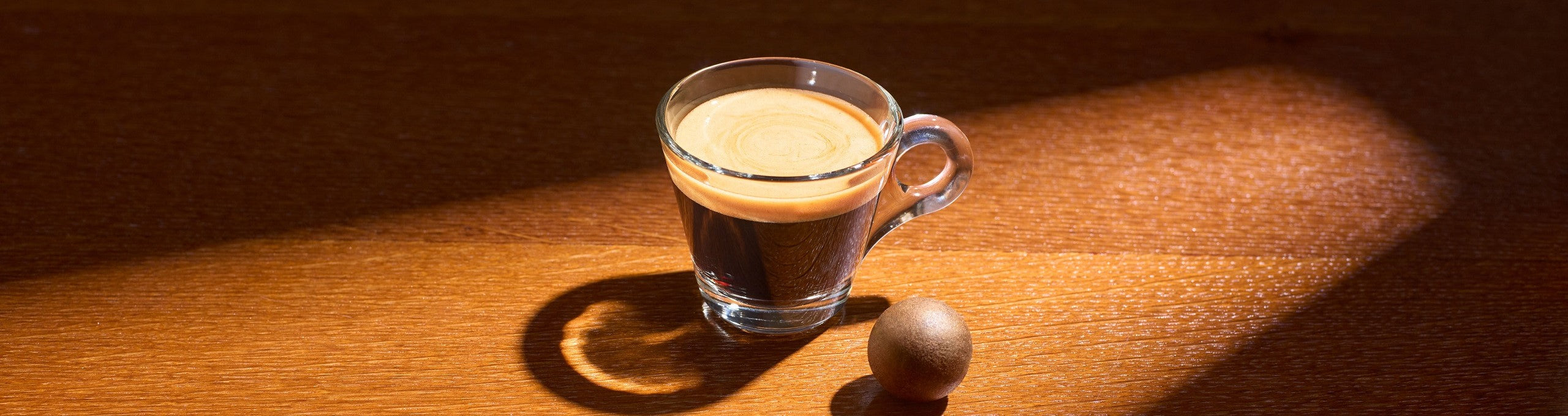 Ein Espresso in einer Glastasse, neben der ein Coffee Ball liegt.