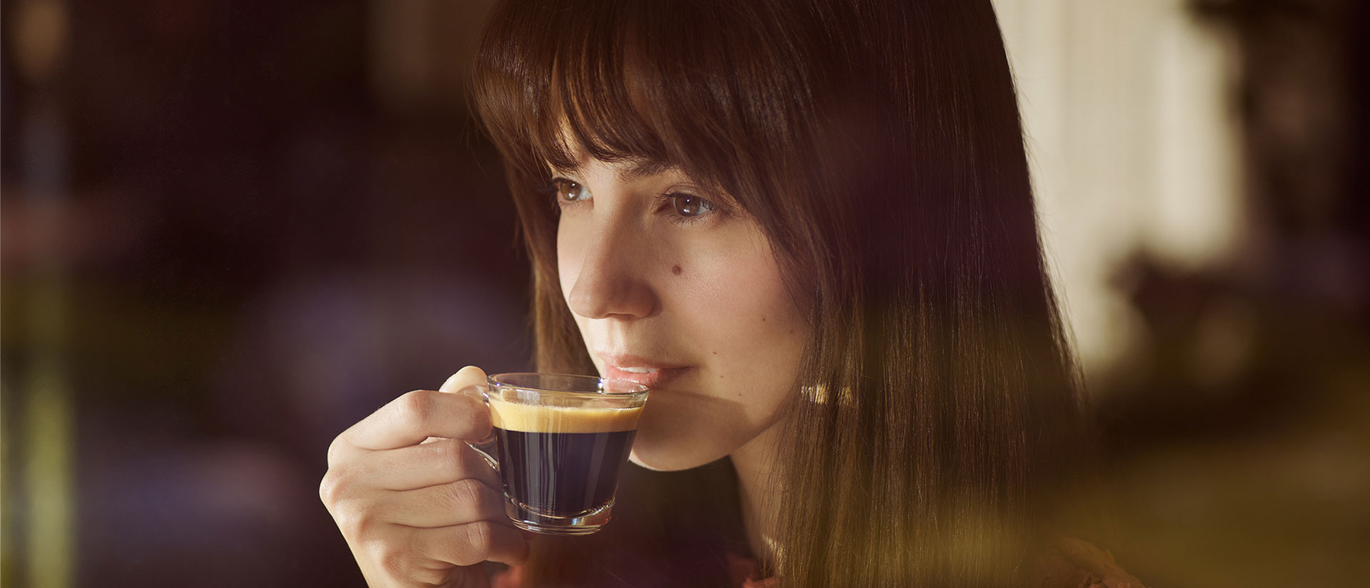 Eine Frau, die einen Espresso in einer Glastasse zum Mund führt